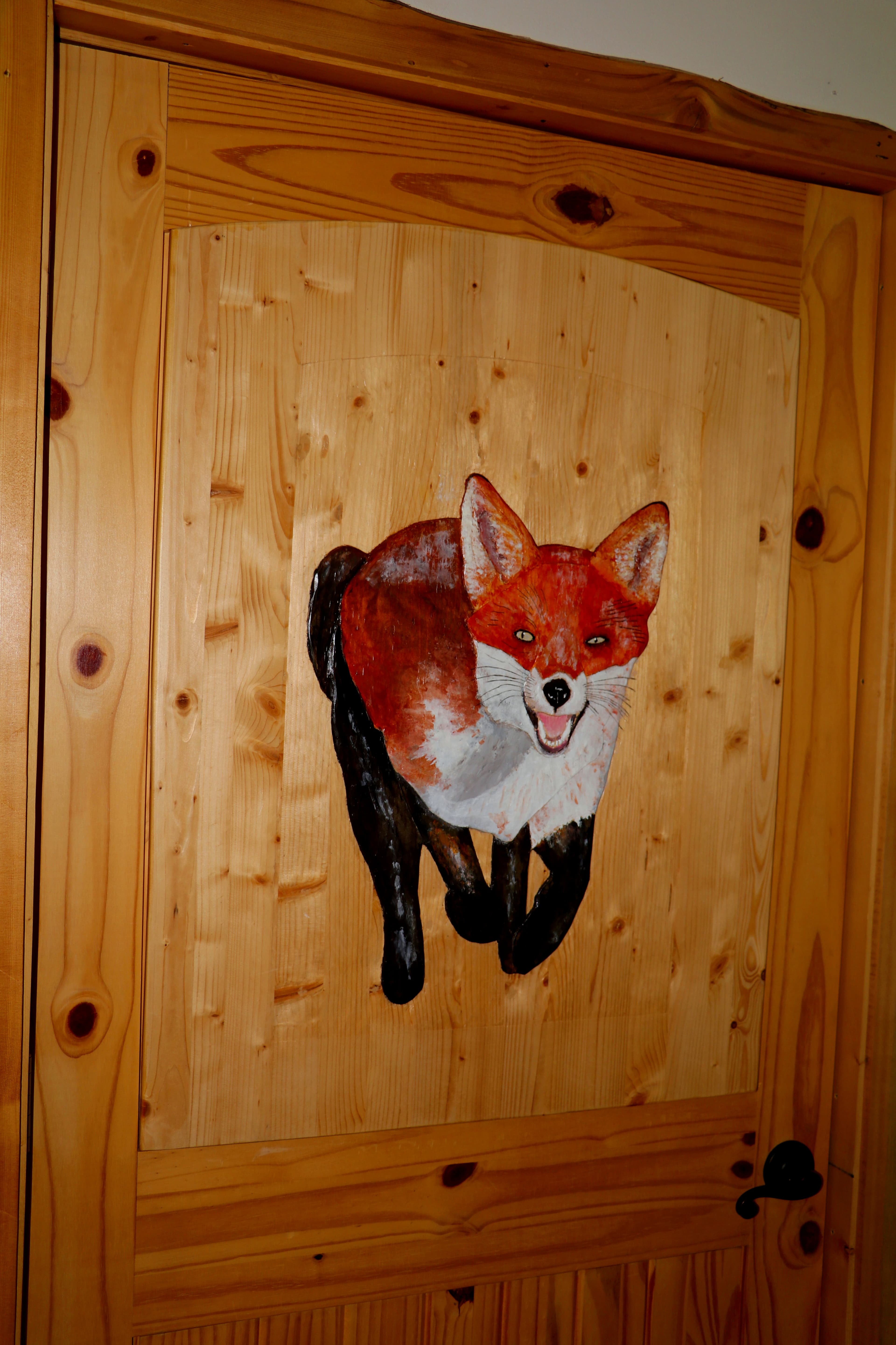 Hand-painted red fox carving on a natural wood door.