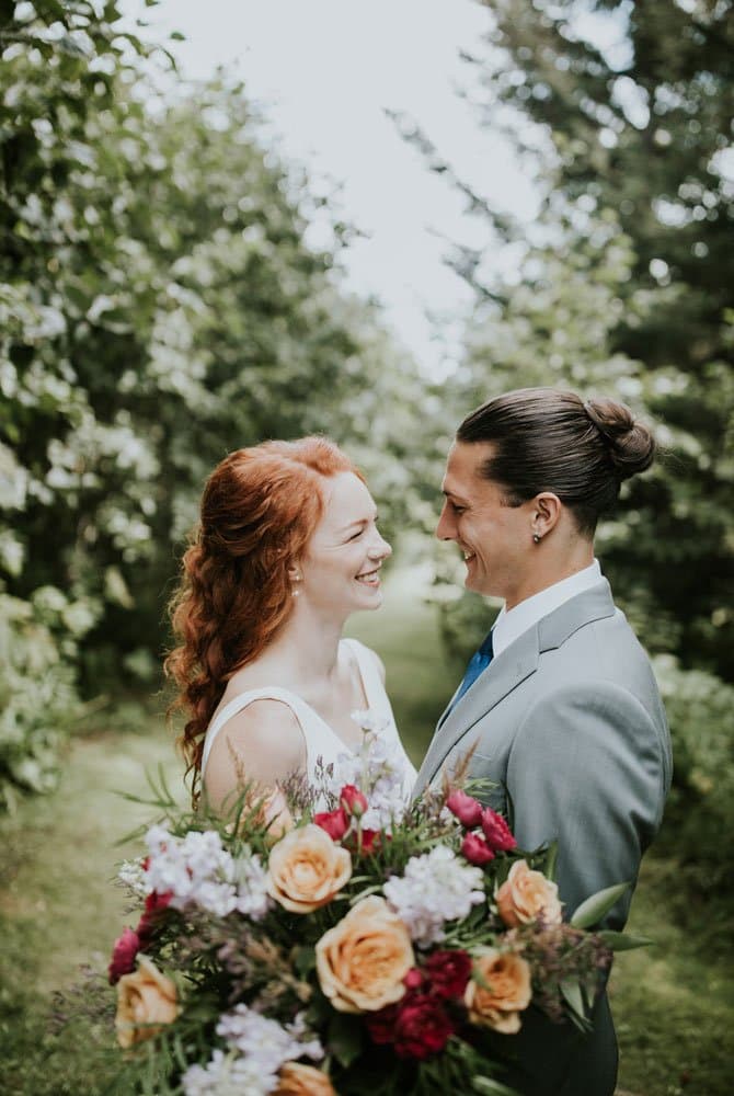 A bride and groom share a joyful moment in a lush garden, with the bride holding a vibrant bouquet.