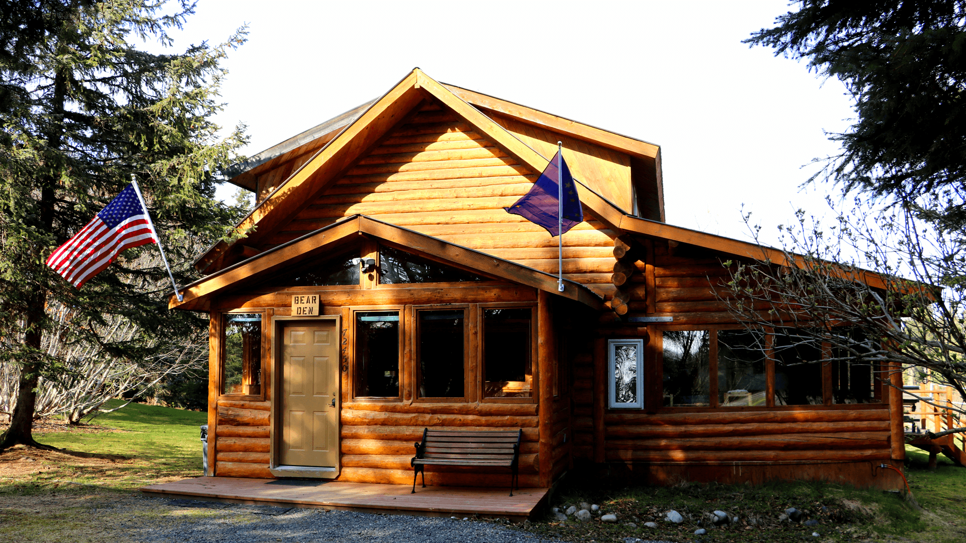 A log cabin with American and Alaskan flags outside.