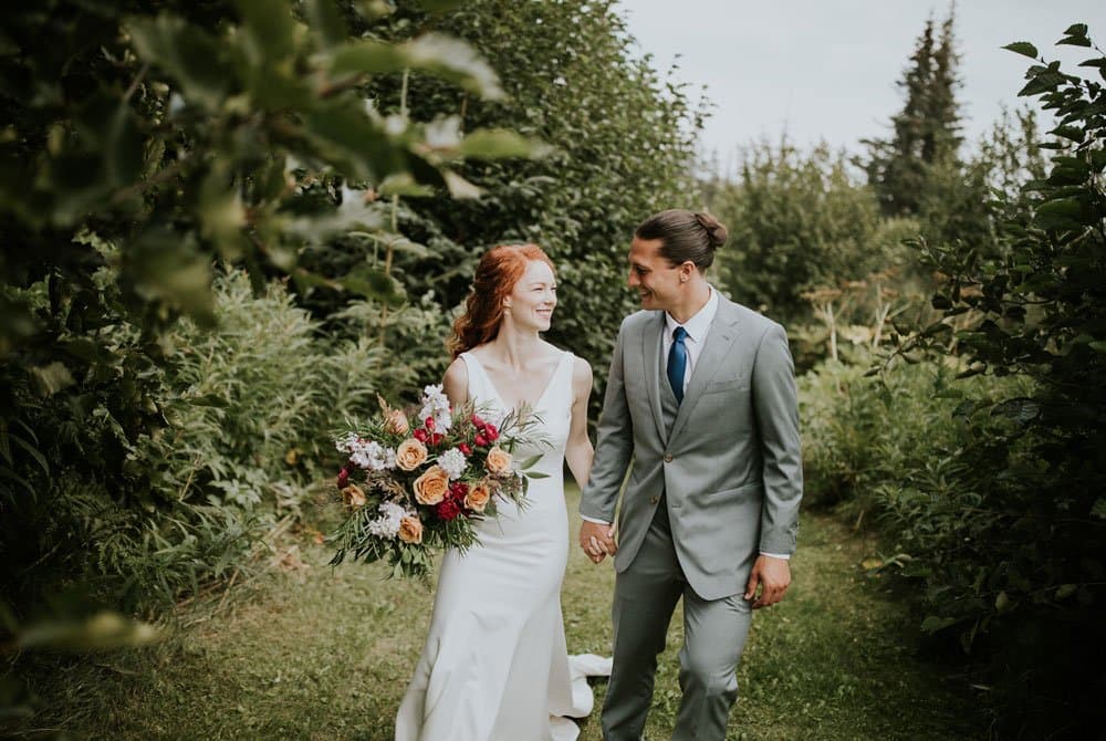 A bride and groom walk hand-in-hand through a lush garden.