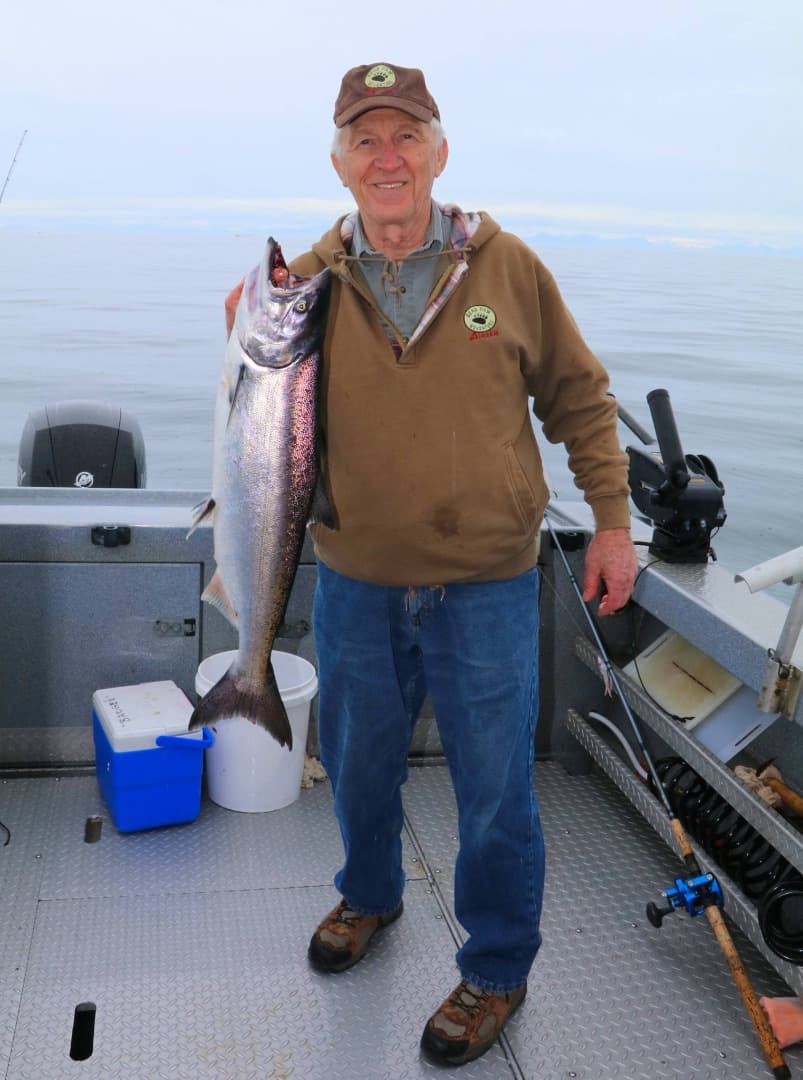 An older man smiles while holding a large fish on a boat.