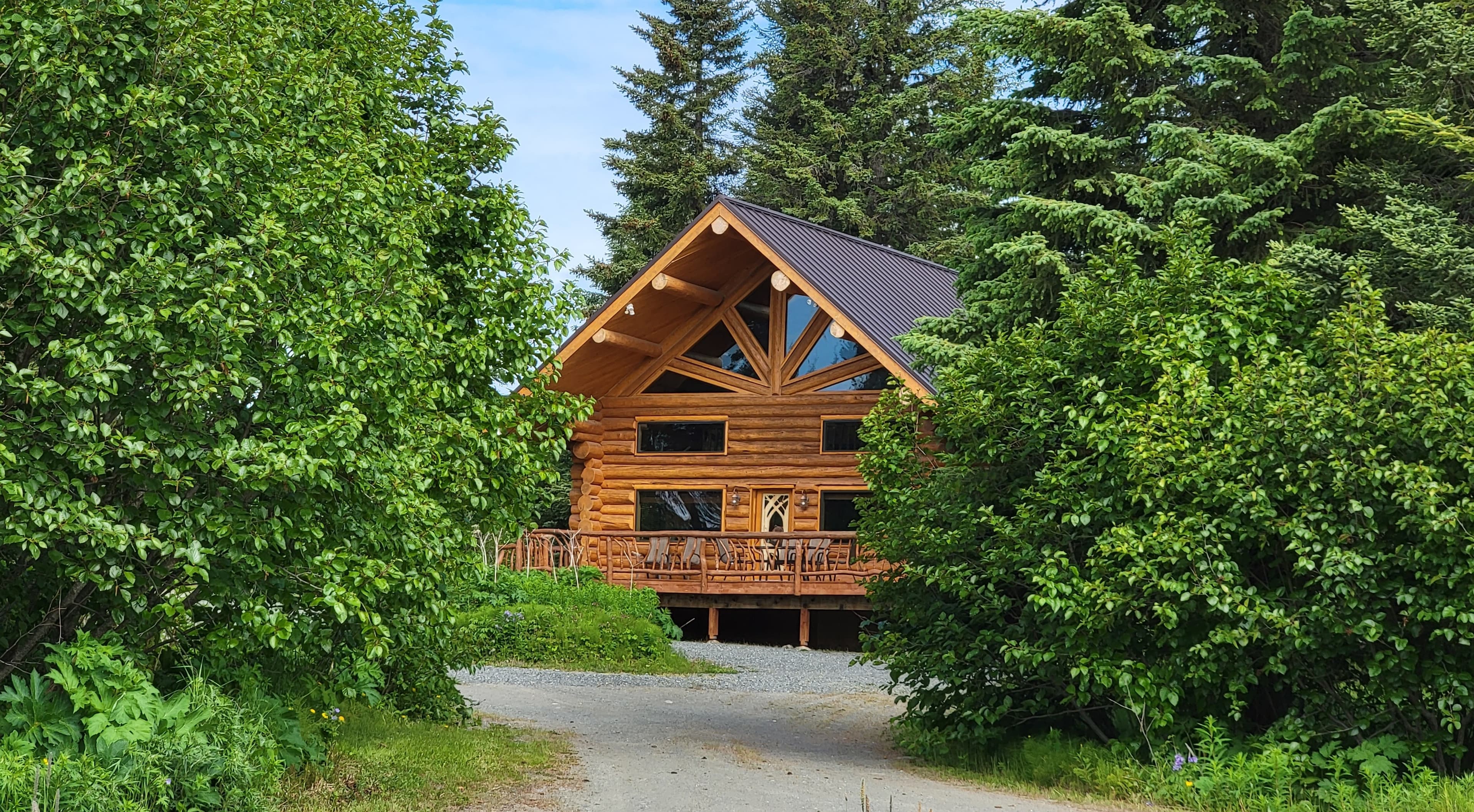 A log cabin with a triangular roof is nestled among lush green trees.