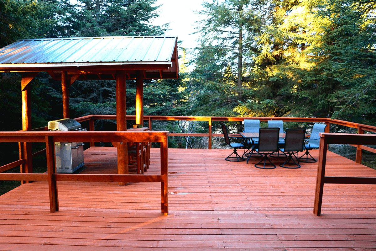 A wooden deck surrounded by trees featuring a barbecue grill and a dining table with chairs.
