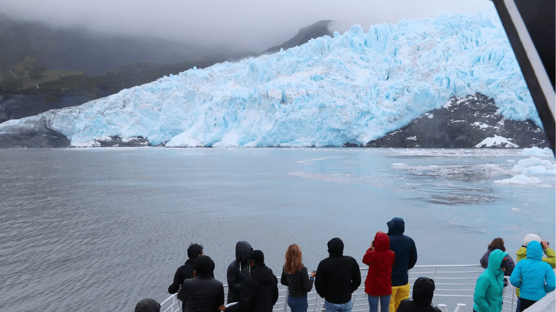 People on a boat in a bay viewing a large, blueish colored glacier