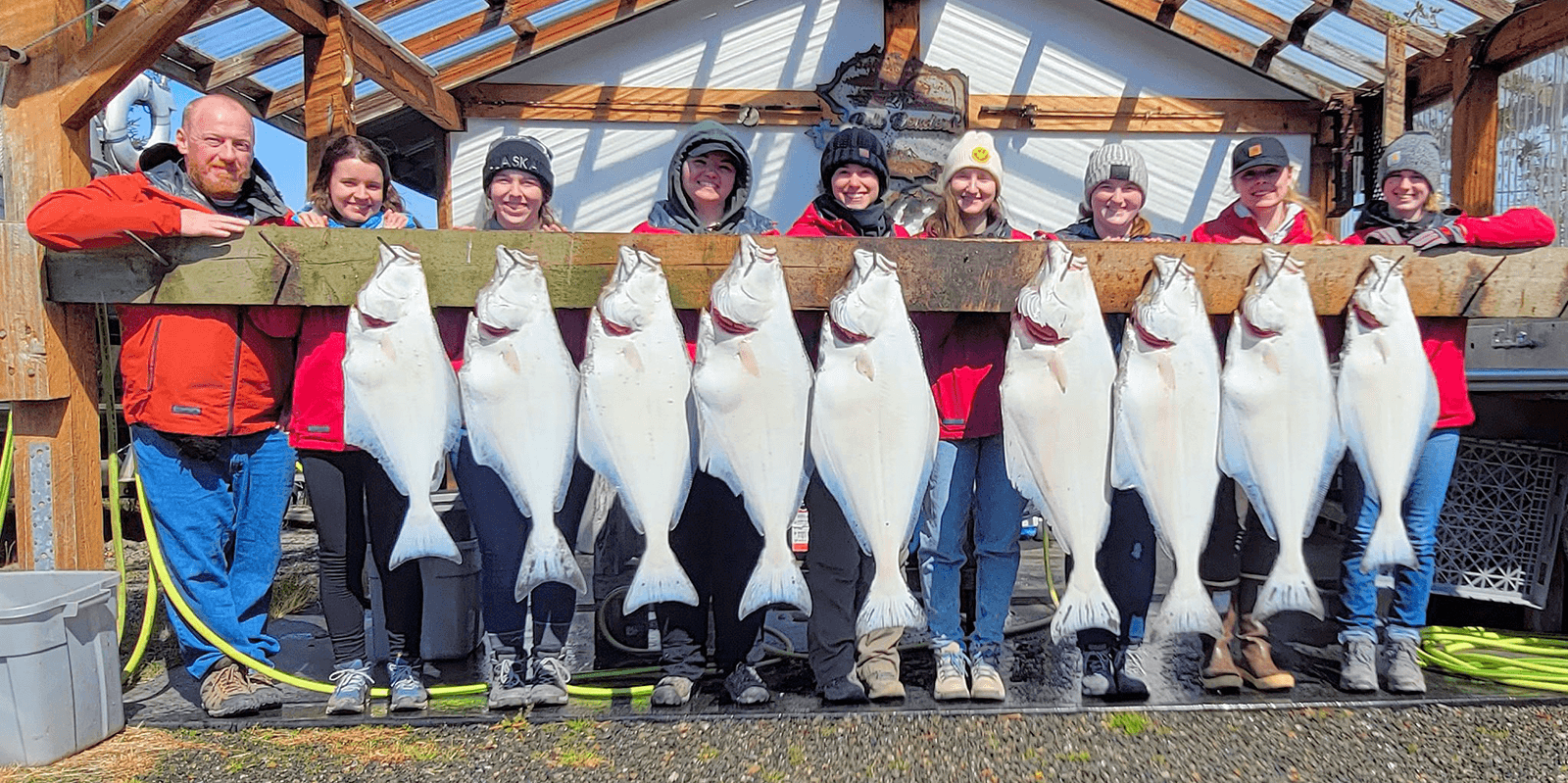 A group of eight people proudly display a line of large halibut caught during a fishing trip.