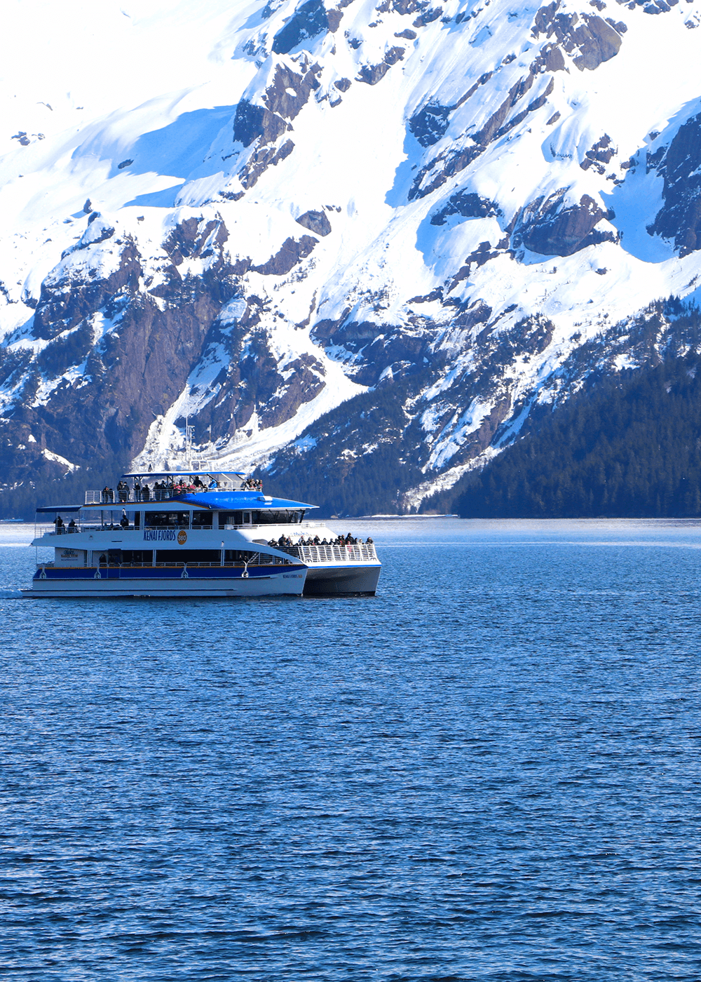 A ferry boat in a body of water with a huge, snow-covered mountain the background