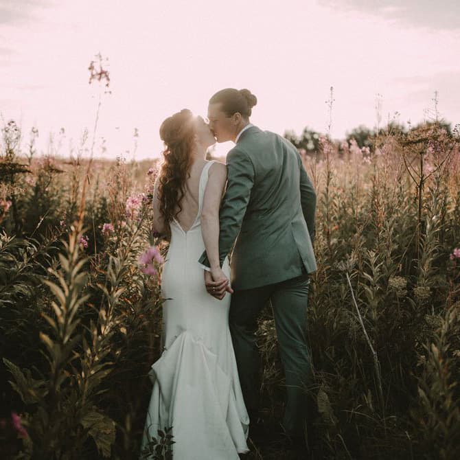 Bride and groom share a kiss in a sunlit field filled with wildflowers.