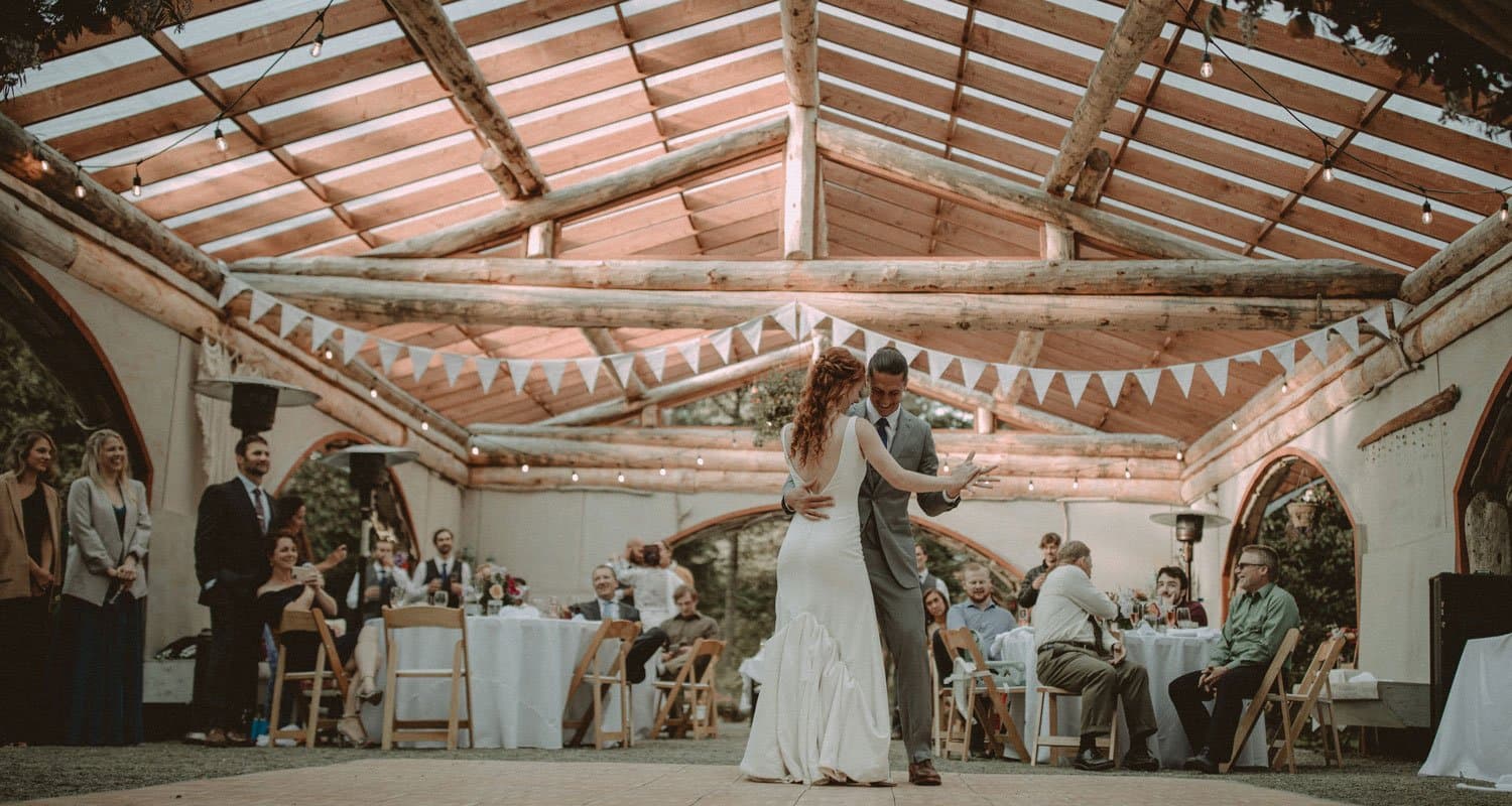 A bride and groom dance together in a rustic venue decorated with bunting while guests observe.