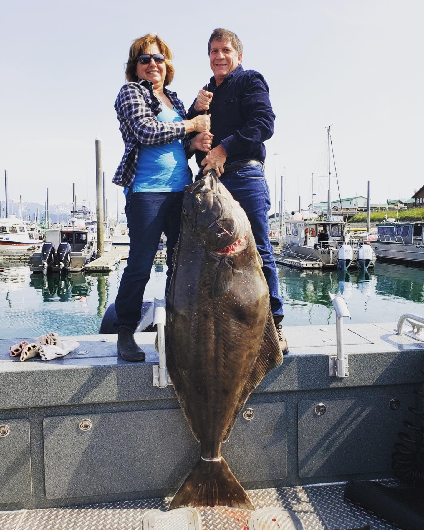 A man and woman proudly hold up a large fish on a boat docked in a marina.